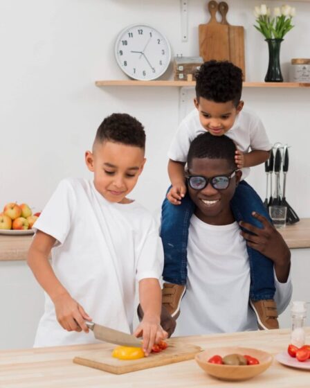 Imagem mostra um pai e dois filhos preparando um jantar juntos