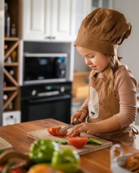 Imagem mostra uma garotinha com roupa de chef na cozinha