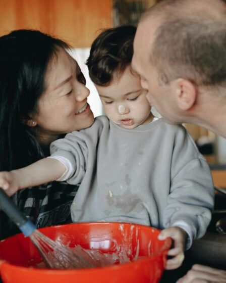 Imagem mostra um filho preparando comida e seus pais fazendo carinho nele