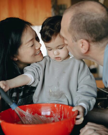 Imagem mostra um filho preparando comida e seus pais fazendo carinho nele