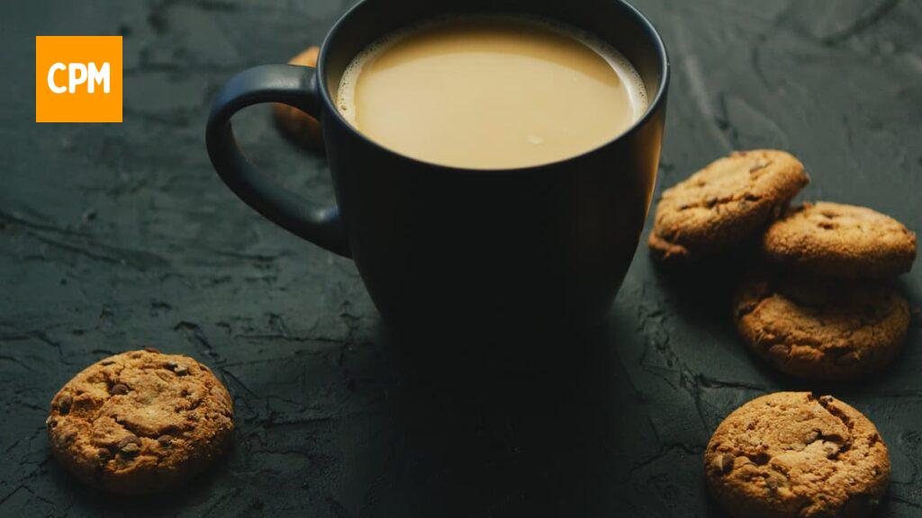 Imagem mostra uma xícara de café com leite acompanhada de um delicioso cookie integral.
