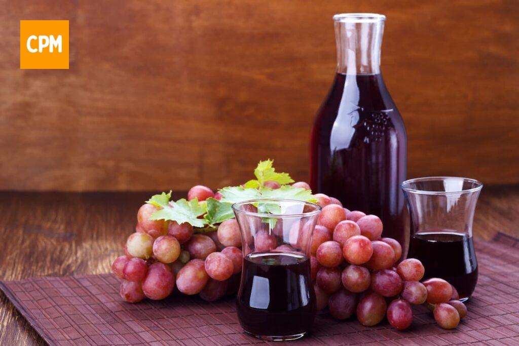 Imagem mostra uva e suco de uva sobre a mesa.