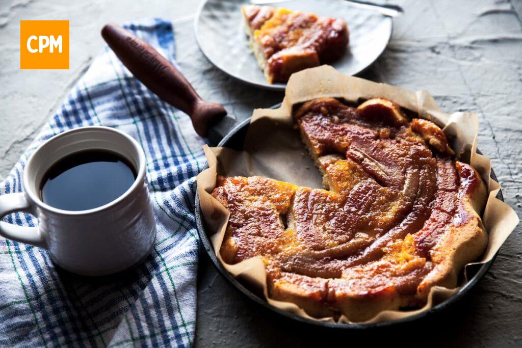 Imagem mostra um saboroso bolo de banana na airfryer com aveia e mel acompanhado de uma linda xícara de café.