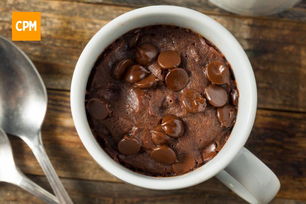 Imagem mostra bolo de banana na caneca com chocolate e gotas de chocolate.