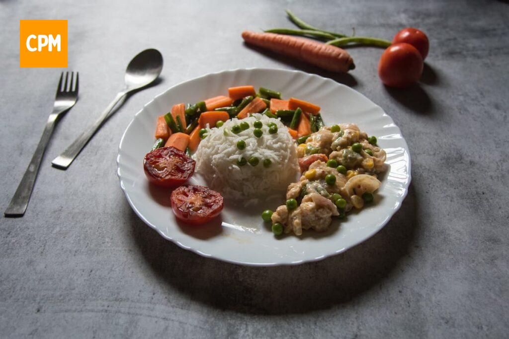 Imagem mostra estrogonofe de frango cremoso servido com arroz branco, tomate  e cenoura.