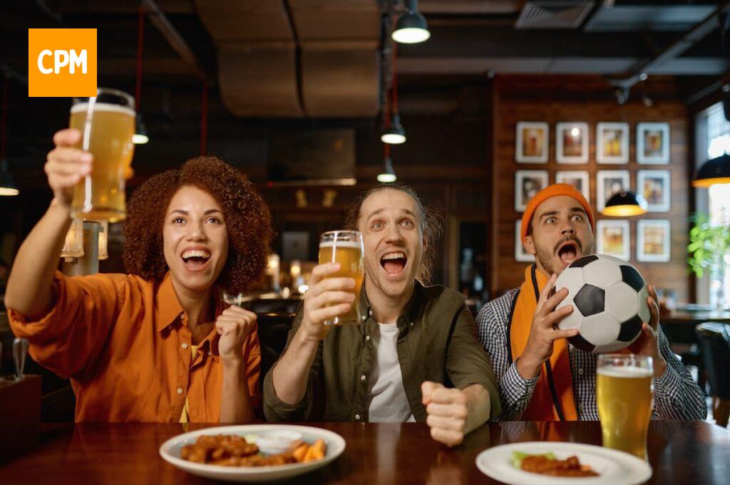 Imagem mostra grupo de amigos comemorando gol em bar.