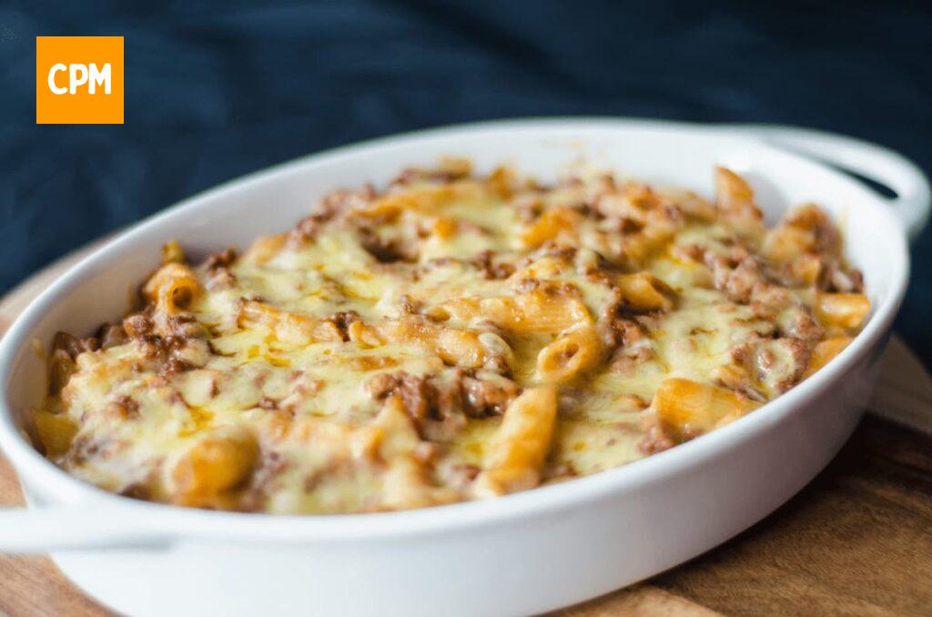Imagem mostra uma travessa de macarrão de forno cremoso com frango e queijo.
